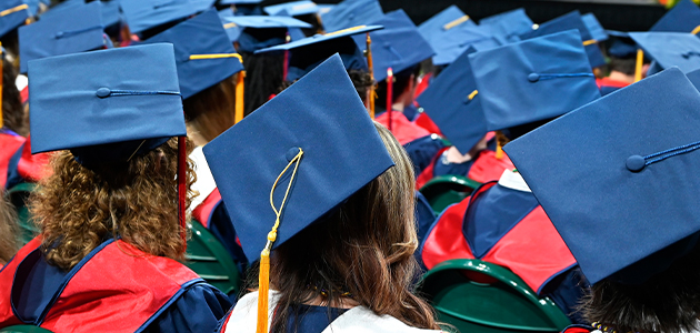 students sitting down in cap and gown at graduation